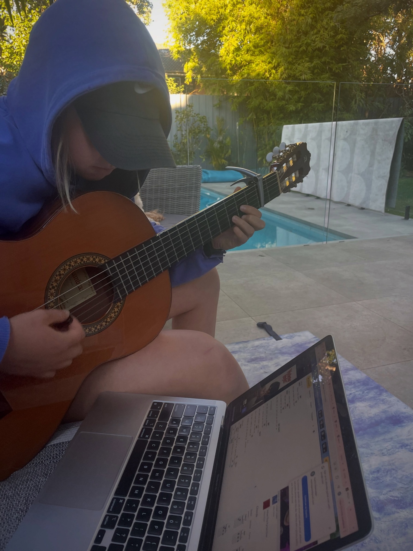 Learning guitar in a hoodie by the pool at golden hour.