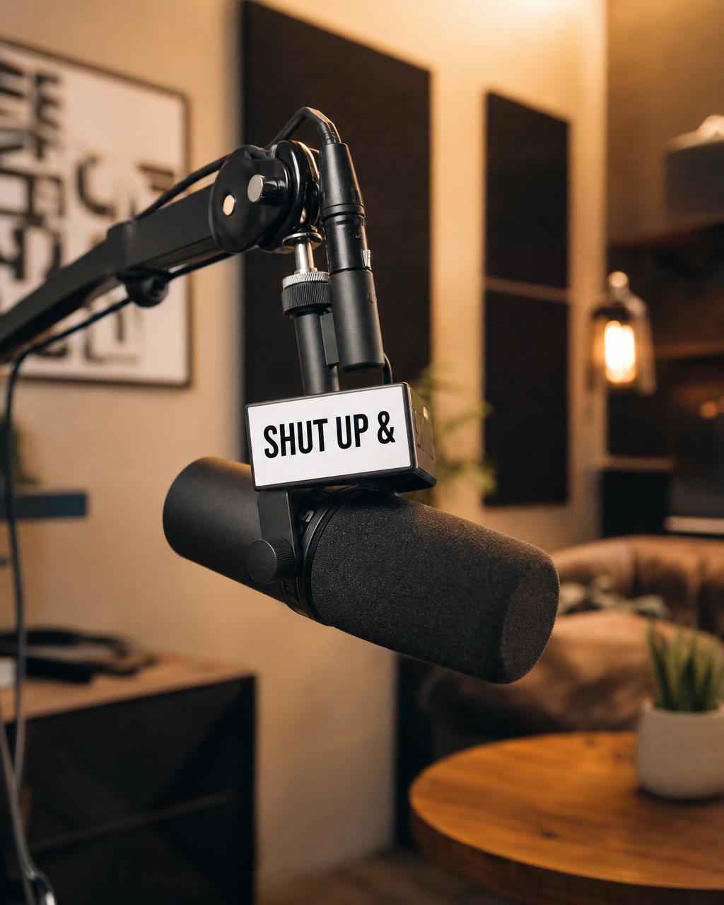 Modern podcast studio microphone with a SHUT UP & mic flag.